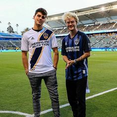 two men standing next to each other on top of a soccer field in front of an empty stadium