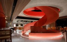 a spiral staircase in the middle of a restaurant with red lighting on it's walls