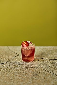 a drink with an apple in it sitting on top of a stone table next to a green wall