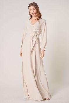 Warm and inviting, the Wholehearted Maxi Dress is a perfect combination of modest and sultry. Long balloon sleeves frame a surplice neckline separated by a tie at the waist, creating a forgiving faux wrap. The skirt maintains an airy and flowy shape that trails behind as you walk down the aisle. - Chiffon- Faux wrap- Keyhole- Elastic waist- Comes in 14 ColorsSize + Fit - Model is 5'9" and wearing size XS- Measurements taken from size S - Chest: 35"- Length: 63 1/4" Fabric Self: 100% PolyesterLin Flowy Long Dress, Taupe Dress, Fashion Ads, Shoulder Ruffle Dress, Wrap Maxi Dress, Long Bridesmaid Dress, Surplice Neckline, Maxi Dress Wedding, Backless Maxi Dresses