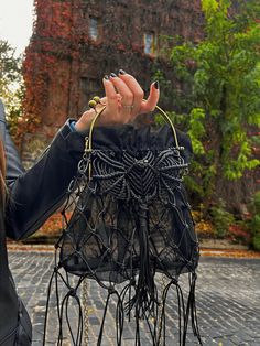 This gothic bag (purse) is made in the shape of a black bat (with rauchtopaz) and is suitable for a party, restaurant or Halloween. It is unique, designed by us and there is only one copy so far. The bag is decorated with fringe and tassels. The accessory is translucent because the inner bag is made of high quality stretch mesh lining that will not wrinkle or fade. The bat is made using the macrame technique and has a convex shape. Bag details: Height - 25 cm/9"  Height with handles - 33 cm/13" Width - 31 cm/12" Depth - 11 cm/4" Color: Black Note that this bag is hand woven and therefore unique. Actual color 🌈 may vary depending on your monitor settings. The size of the bag may vary slightly, as we do not have mass production and each bag is made by hand.  We are happy to answer any quest Bat Girl Costume, Dragon Dice Bag, Goth Purse, Bat Girl, Gothic Bag, Batgirl Costume, Macrame Purse, Halloween Candy Bags, Dragon Dies