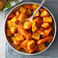 a white bowl filled with cooked carrots on top of a blue towel next to a spoon