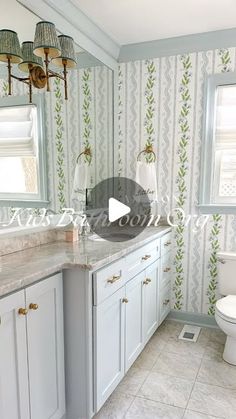 a bathroom with white cabinets and marble counter tops, along with wall papered walls