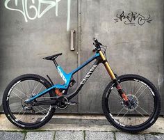 a blue and black mountain bike parked in front of a wall with graffiti on it