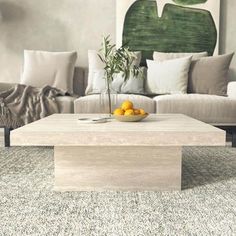 a coffee table with fruit on it in front of a couch and painting behind it