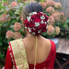 a woman wearing a red and gold sari with flowers in her hair is seen from the back