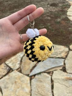 a hand holding a yellow and black keychain with a white pom - pom on it