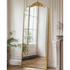 a large gold framed mirror sitting on top of a wooden floor next to a window