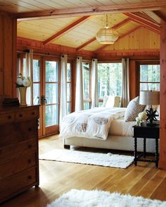 a bedroom with wooden walls and white bedding in the center, along with large windows