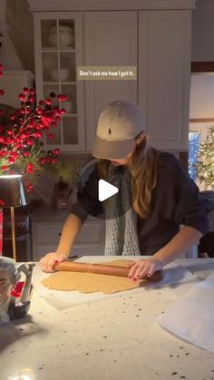 a woman is rolling out dough on a table with christmas decorations in the back ground