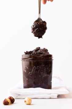 a spoonful of chocolate pudding being lifted from a jar with nuts on the side