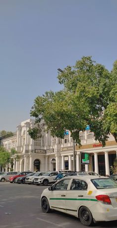 cars are parked in front of a large white building with columns on the top floor