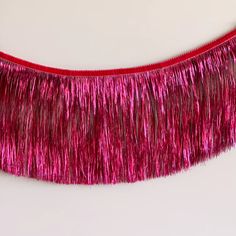 a red fringe hanging from the side of a white wall with pink tinsel on it