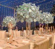 the tables are set with white flowers and candles for an elegant dinner or reception at night