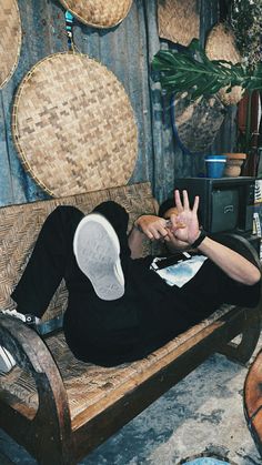 a man laying on top of a wooden bench in front of a wall with baskets