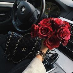 a woman's hand is holding flowers in her purse while sitting in the driver's seat of a car