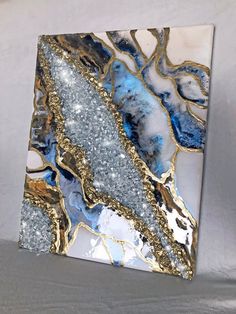 an abstract painting with blue, gold and white colors on the canvas is hanging on a wall