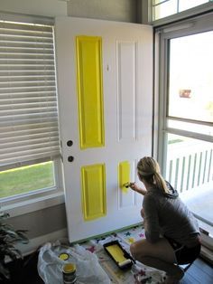 a woman is painting the front door of a house with yellow paint and white shutters