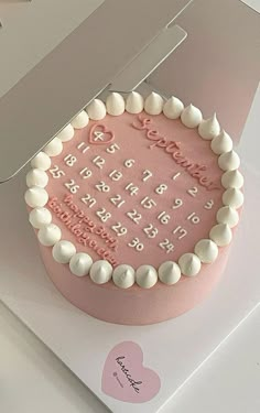 a pink birthday cake with white frosting and hearts on the top is in a box