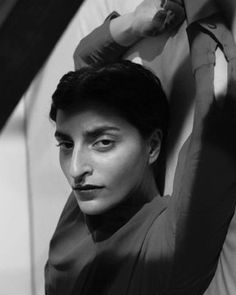 black and white photograph of a woman leaning against a wall with her hands behind her head