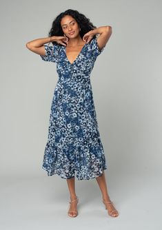 A dreamy mid-length button-front chiffon dress in an indigo blue and navy floral print. Floral print Chiffon Relaxed fit Short sleeves Mid-length Tiered skirt V-neckline Self-covered button front Adjustable back waist tie Sheer Lined Bohemian midi dress Lightweight chiffon lends an ethereal touch to this dreamy spring midi dress. Designed in a floral print, with short sleeves, a self-covered button front, and a flattering v-neckline. An adjustable tie at the back adds waist definition. Model is Blue V-neck Midi Dress With Ditsy Floral Print, Blue Flowy V-neck Floral Dress, V-neck Blue Dresses With Ditsy Floral Print, Blue V-neck Dress With Ditsy Floral Print, Blue Flowy Midi Dress With Surplice Neckline, Blue V-neck Floral Dress With Ditsy Print, Bohemian Blue Midi Dress With Ditsy Floral Print, Indigo V-neck Maxi Dress For Spring, Spring Indigo Floral Print Dress