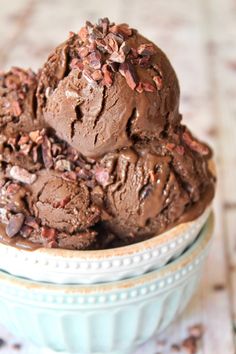 two scoops of chocolate ice cream in a blue bowl on a table with pecans