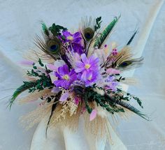 a bouquet with purple flowers and feathers on a white tableclothed cloth, ready to be used as a centerpiece