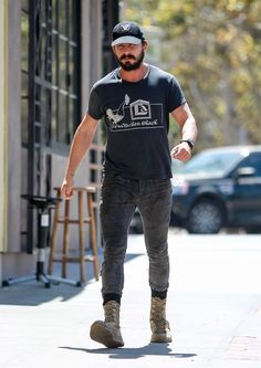 a bearded man walking down the street with his foot in the air while wearing a hat