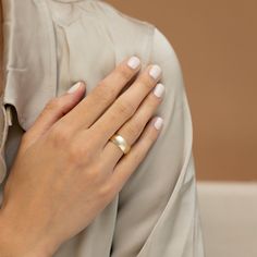 a woman's hand with a gold ring on her left wrist, and white nails