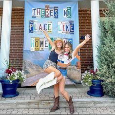 two women are posing in front of a sign for there's no place like home