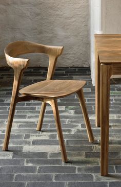 a wooden chair sitting next to a table on top of a brick floor in front of a white wall