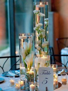 two tall vases filled with flowers and candles on top of a dining room table