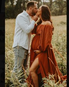 a pregnant couple kissing in the middle of a field