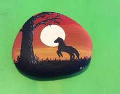 a painted rock with a horse standing in front of a tree and the moon behind it