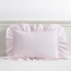 a pink pillow with ruffled edges sitting on a white floor next to a wall