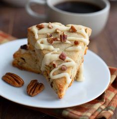 two pieces of cake with frosting and pecans on a plate next to a cup of coffee