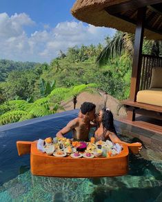 a man and woman sitting in a boat with food on the bottom, surrounded by greenery