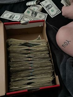 a box full of money sitting on top of a bed next to a person's stomach