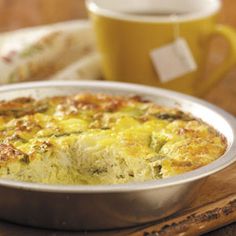 a close up of a casserole in a pan on a wooden table next to a cup