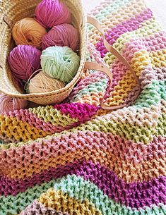 a basket filled with balls of yarn sitting on top of a floor next to a blanket