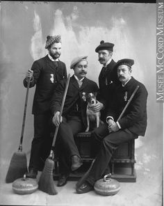 an old black and white photo shows three men with brooms, one holding a dog