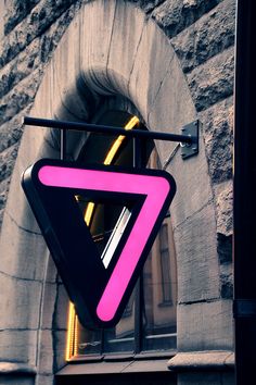 a neon pink triangle sign hanging from the side of a building