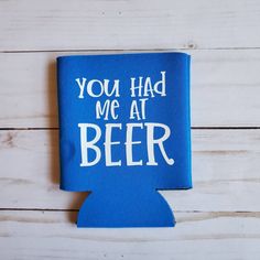 a blue can cooler with the words you had me at beer printed on it sitting on a wooden surface