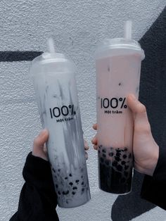 two people holding up their drinks in front of a wall with the words 100 % written on it