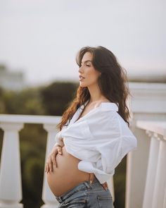 a pregnant woman standing on a balcony with her hands on her hips and looking off to the side