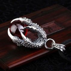 This Dragon's Gem necklace depicts a dragon claw grasping a priceless gem from its hoard. Made with stainless steel, this striking necklace is great gift for loved ones who also enjoy dragons and fantasy.Materials: Stainless Steel, Synthetic Crystal Pendant Size: 4.3 x 2.0 cm (1.7" x 0.7")Chain Length: ~50cm (19.6") Click ADD TO CART To Order Yours Now! The Checkout Process is Guaranteed to be 100% Safe and Secure with Visa, Mastercard, AMex, Discover, Apple Pay or PayPal. Gothic Claw Shaped Jewelry Gift, Fantasy Materials, Dragon Jewelry Necklace, Metal Jewelry With Dragon Design As Gift, Gothic Claw Jewelry For Gifts, Metal Jewelry With Dragon Design For Gift, Gothic Claw Jewelry Gift, Dragon Necklace Aesthetic, Metal Dragon Design Jewelry Gift