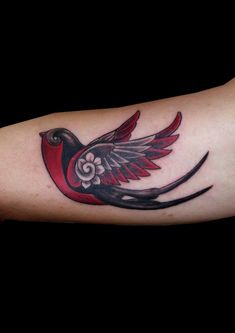 a red bird with black wings and flowers on it's arm, done by tattoo artist