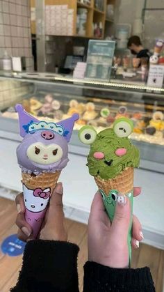 two people holding up ice cream cones with animals on them