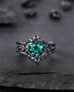 a ring with an emerald colored stone in the center on top of a black rock