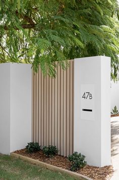 a white wall with a wooden fence next to it and some plants on the ground